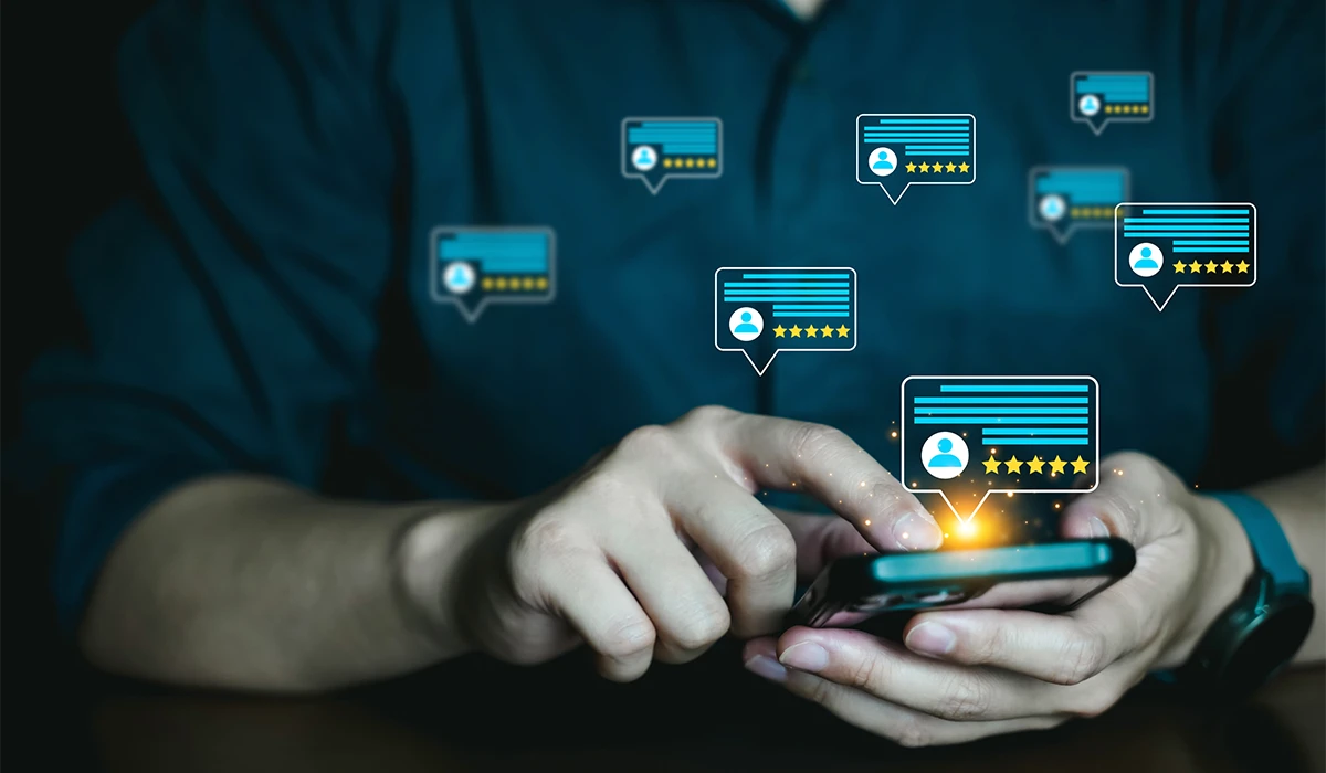 A person using a smartphone with digital speech bubbles floating above the screen, each displaying five-star ratings and user profiles to represent data from Customer Satisfaction Surveys.