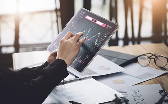 Close-up of a person touching a tablet screen showing financial trend charts, surrounded by printed reports, highlighting data analysis for our ethnography work.