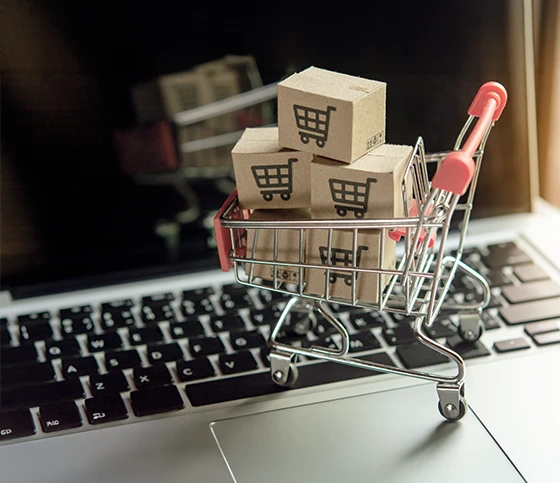 Close-up of small cardboard boxes in a mini shopping cart on a laptop for e-commerce mystery shopping audit
