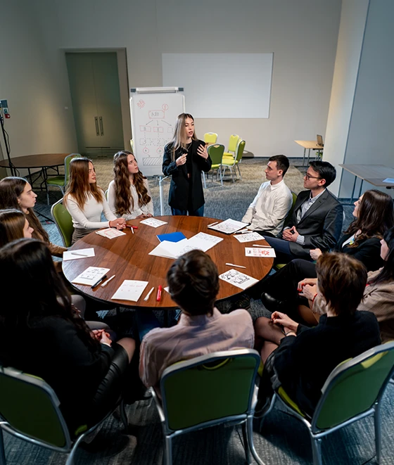 A group of people sitting around a circular table listening to a presenter during a central location testing market research session.